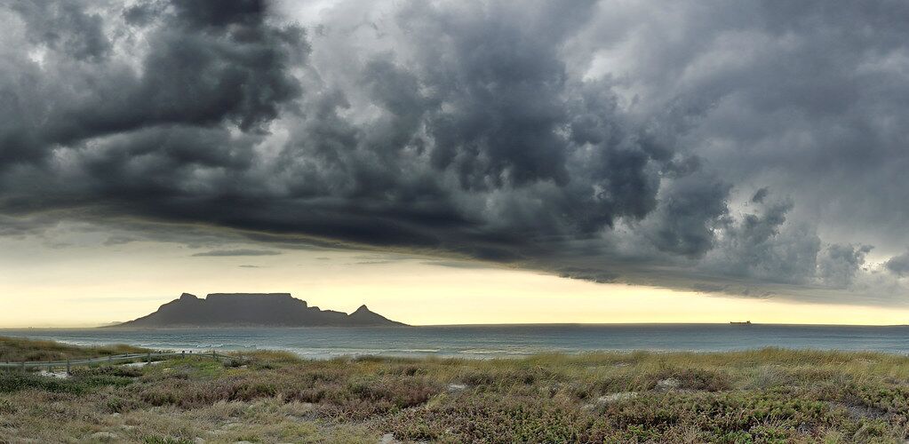 Table Mountain under a dark, dramatic sky at dusk, seen across Table Bay